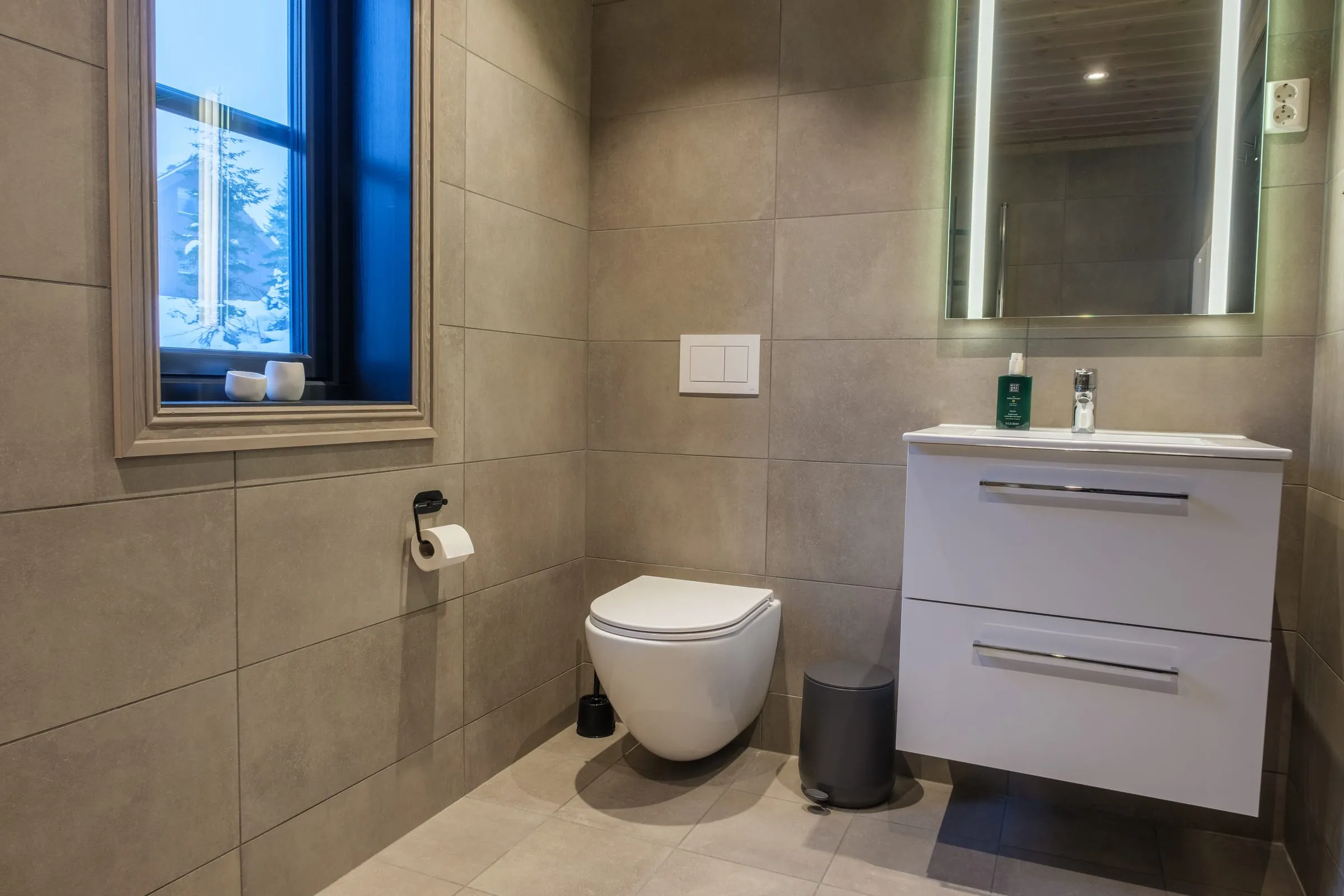 Tiled bathroom with a backlit mirror and a window to the snow