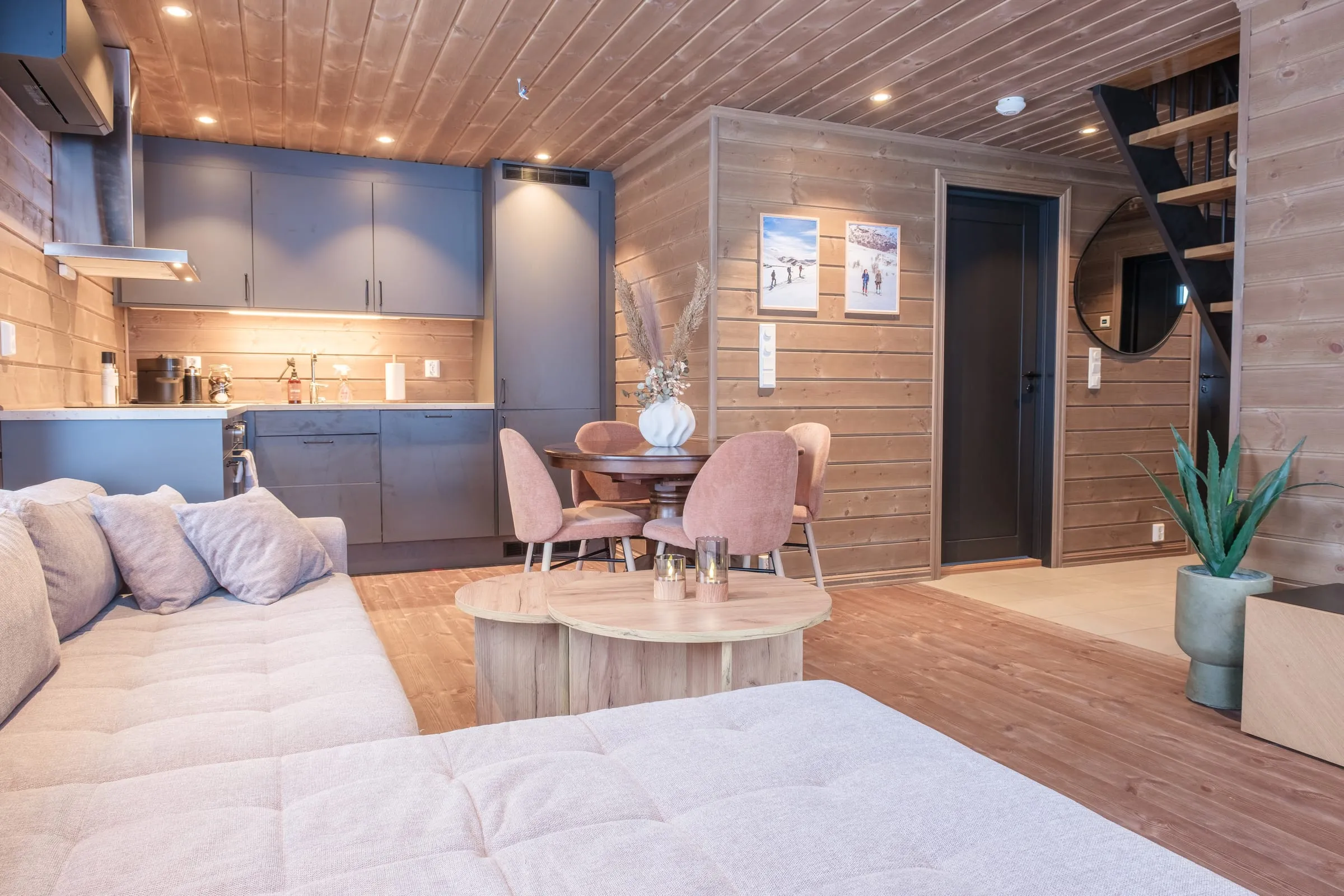 Open-plan living room with slate-blue kitchen, warm pine walls and a round oak table